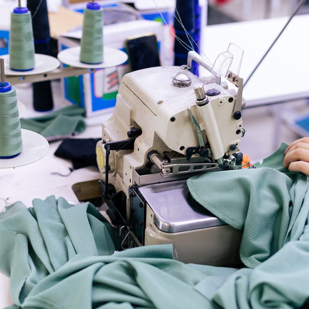 Personne qui coud un tissu vert dans une usine de fabrication textile